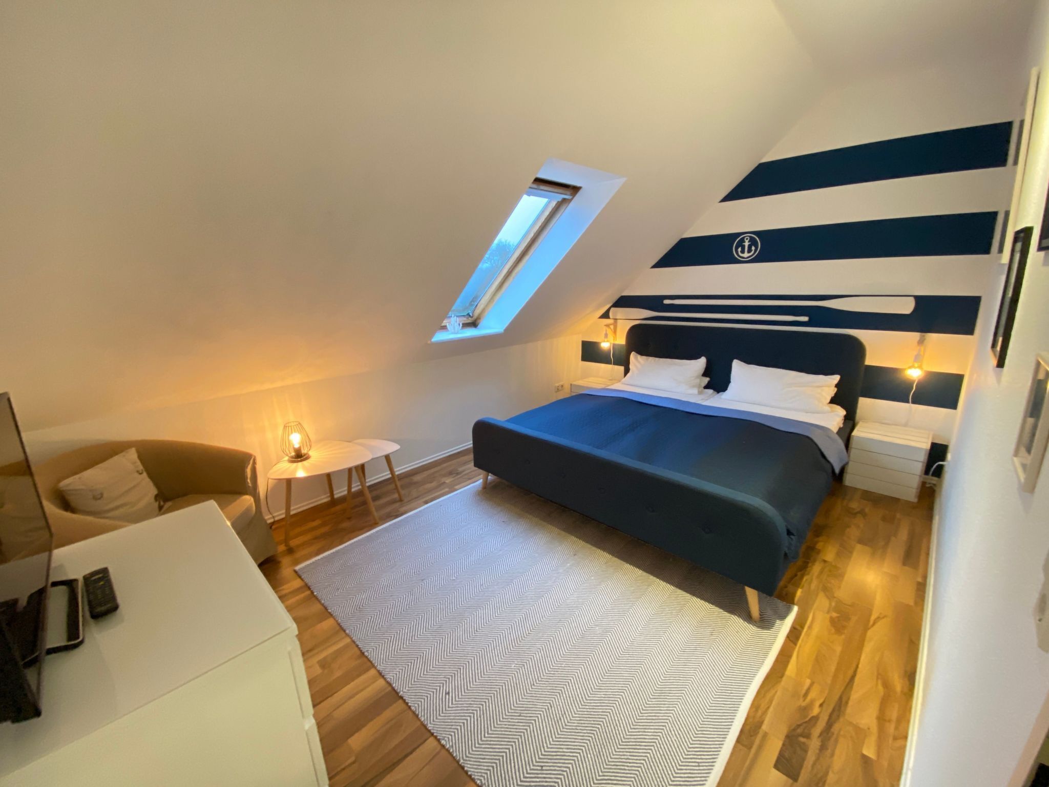 A bedroom with a skylight, a bed, bedside tables, a chair, and a patterned rug.