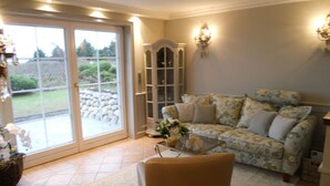 Uma sala de estar com sofá, mesa de centro de vidro, poltrona, armário e uma grande porta de correr que dá para um jardim.