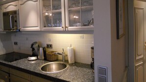 Cozinha com armários brancos, pia de aço inoxidável e micro-ondas.