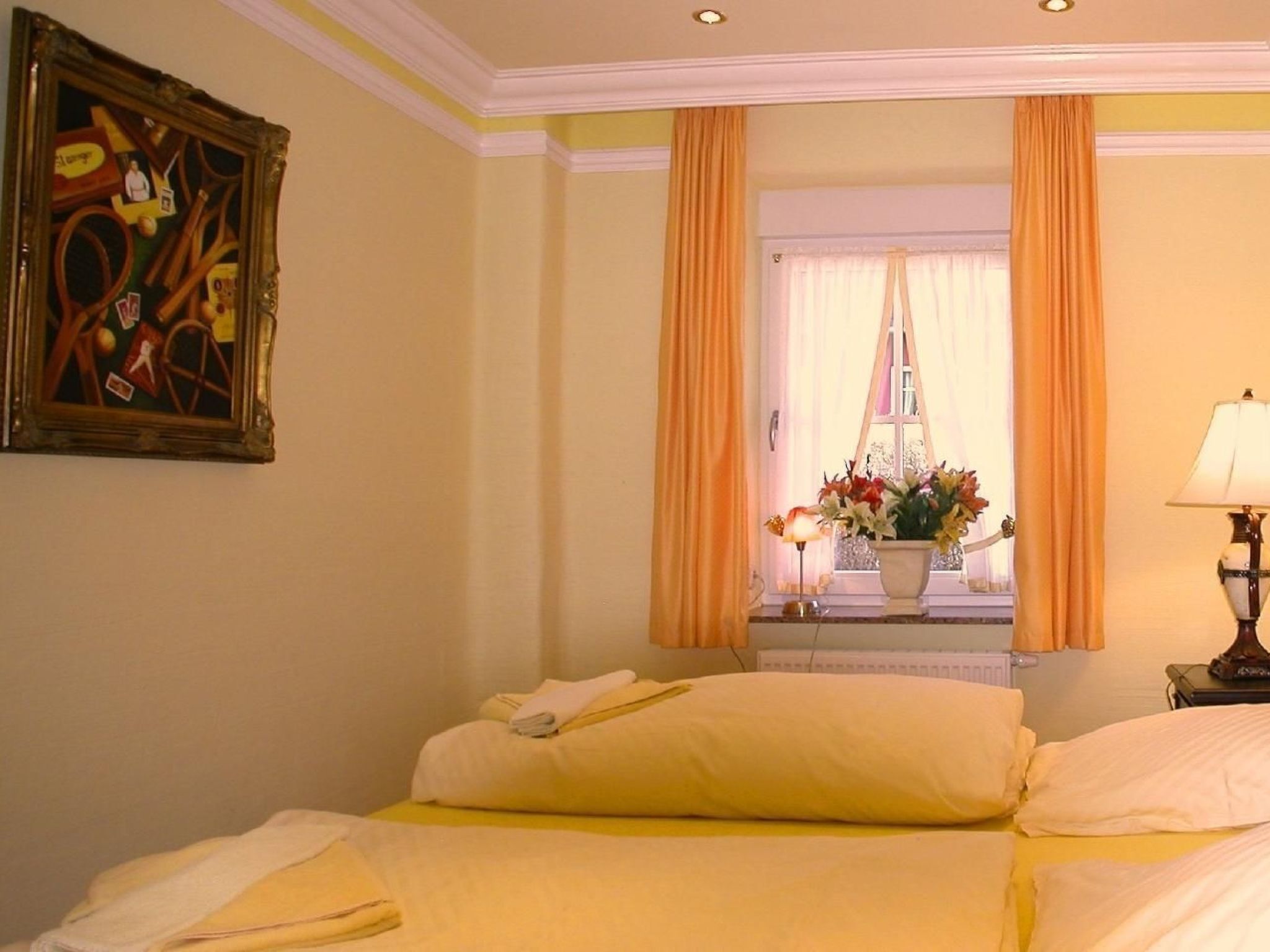 A hotel room with two beds, a painting on the wall, a window with curtains, and a lamp on a bedside table.