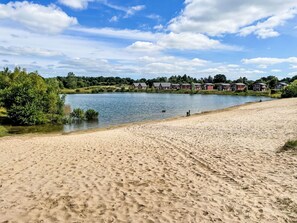 A sandy beach with footprints, a calm lake, and houses in the background.