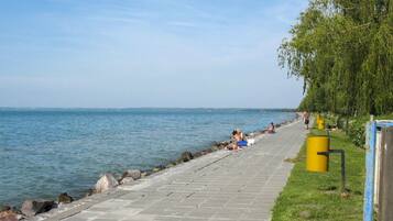 A paved walkway beside a body of water, with people relaxing and walking.