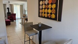 Un comedor con una mesa y sillas, un cuadro colgado en la pared con pasta, y una pequeña planta en maceta sobre la mesa.