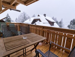 Una terraza de madera con una mesa y sillas, con vista a un edificio cubierto de nieve.