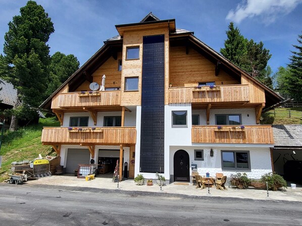 Un edificio de madera de dos pisos con balcones, un garaje y mobiliario exterior.