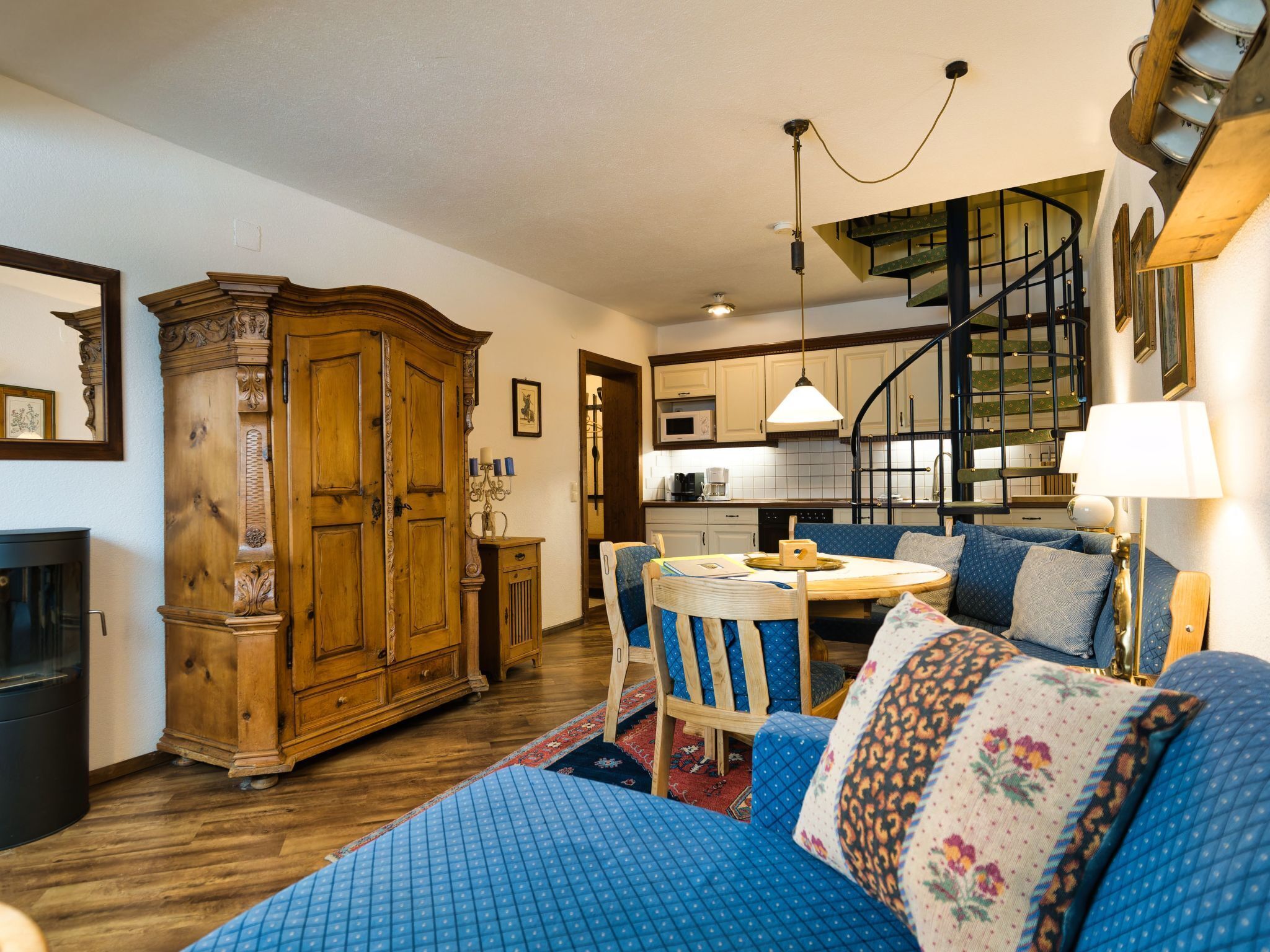 Ein gemütliches Wohnzimmer mit einem großen Holzschrank, einem blauen Sofa und einem Essbereich mit Tisch und Stühlen.