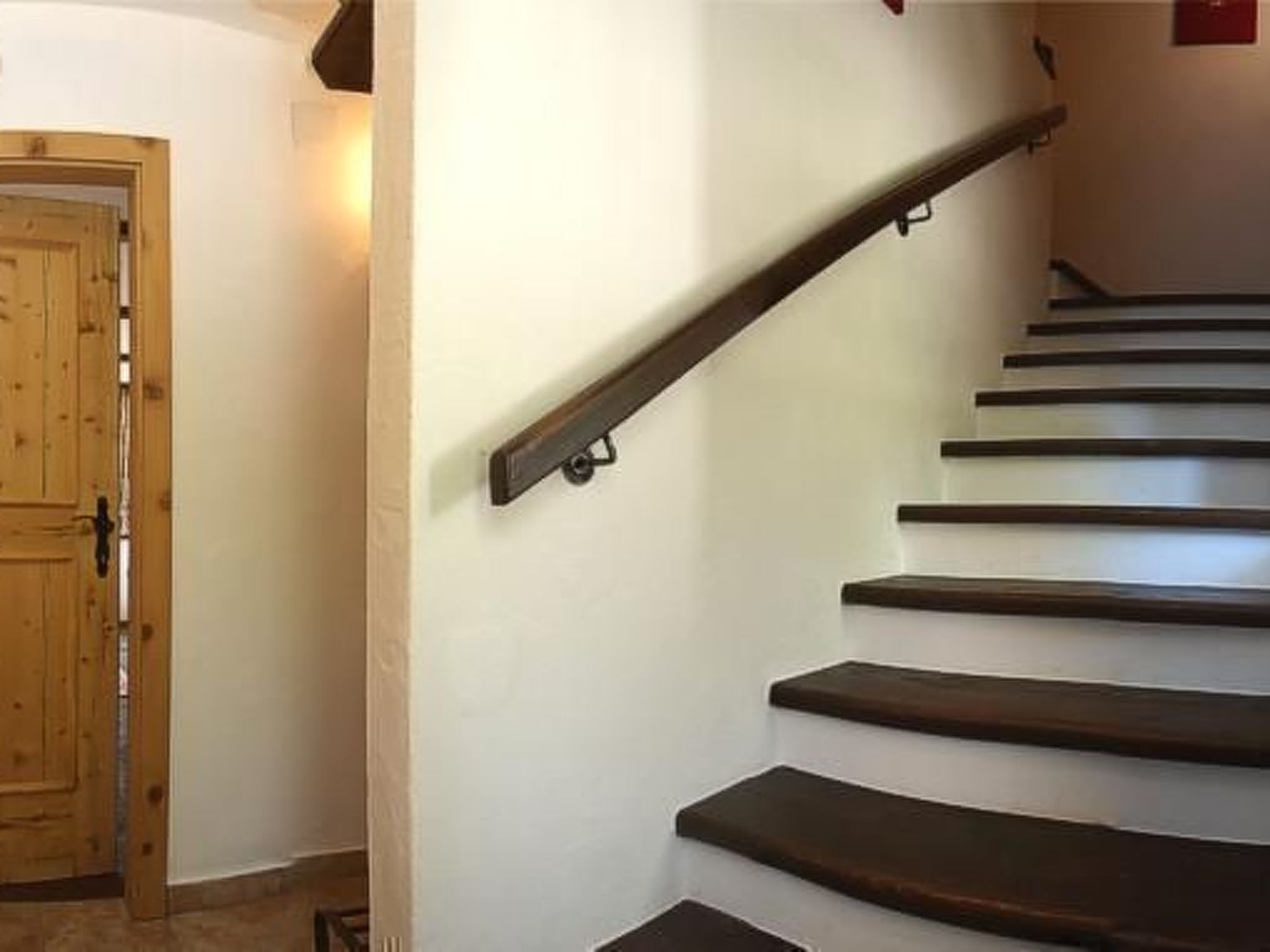 A wooden door with a black handle and a staircase with dark wooden steps and a metal handrail.