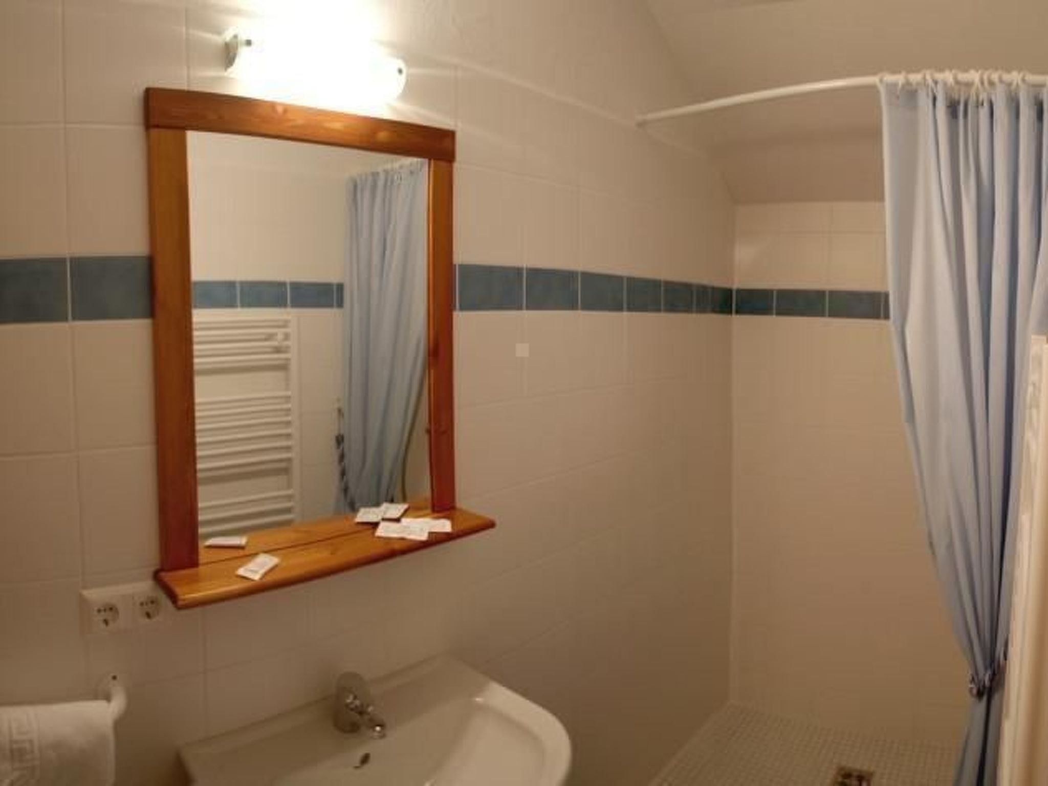 Une salle de bain avec un miroir encadré en bois, un lavabo blanc et un rideau de douche.