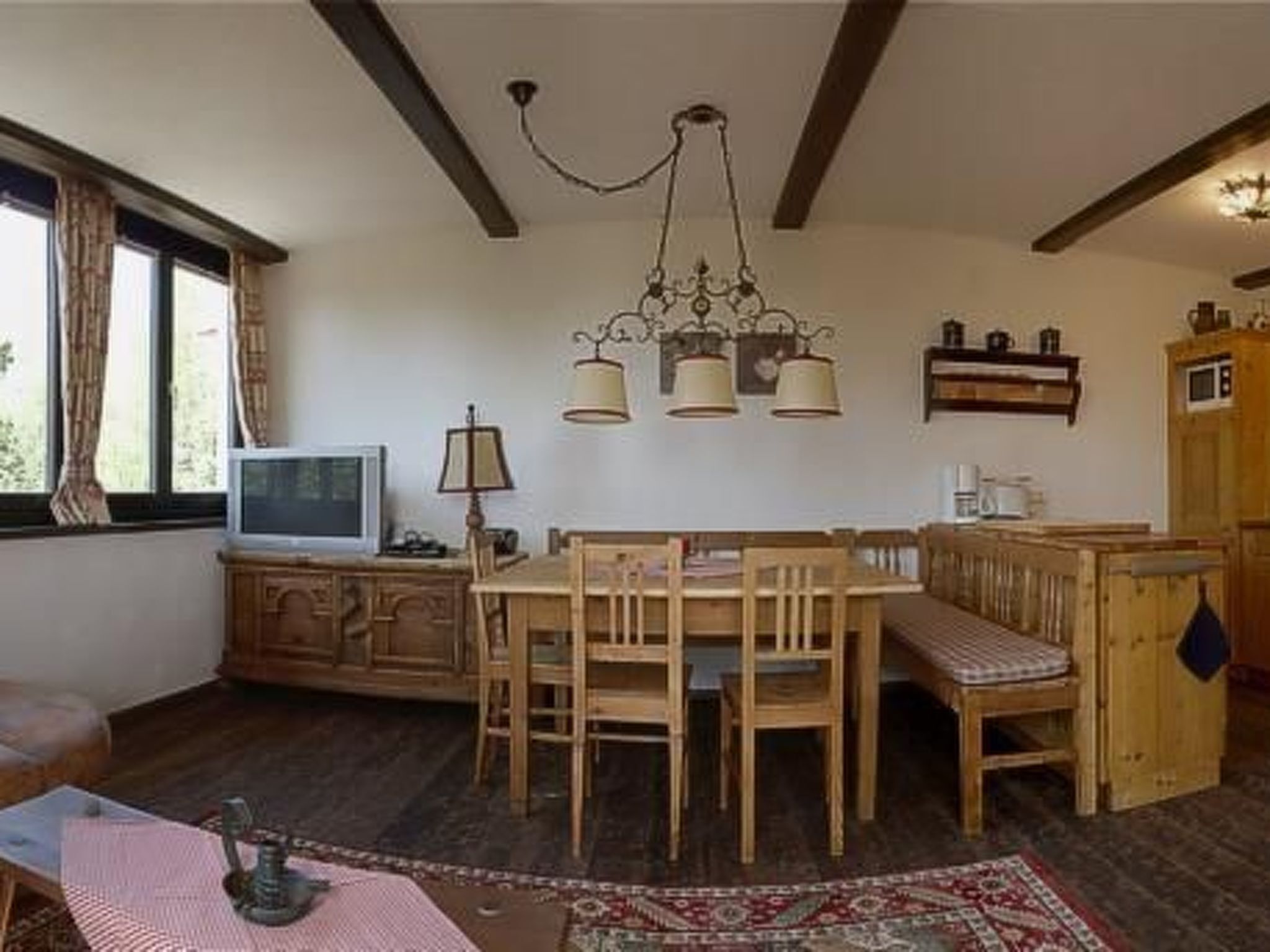 Un salon chaleureux avec une table à manger en bois, des chaises, un téléviseur, une lampe et un tapis à motifs.