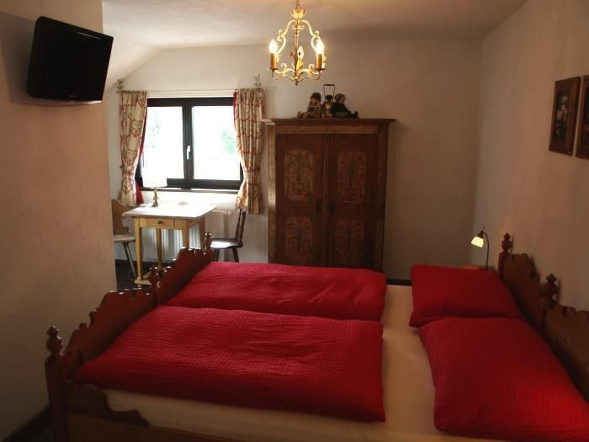 Ein Schlafzimmer mit einem Doppelbett, einem Holzschrank, einem Schreibtisch mit Stuhl und einem an der Wand befestigten Fernseher.