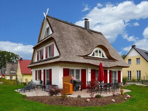 A traditional house with a thatched roof, red shutters, and a small outdoor seating area with chairs and a table. - Villa Lhamo by Interhome (Glowe)