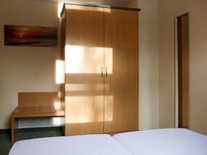 Habitación de hotel con un armario grande de madera, una cama, un banco y un cuadro en la pared.
