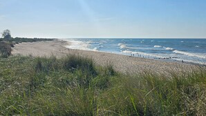Ein Strand mit blauem Himmel, Wellen und grasbewachsenen Dünen.