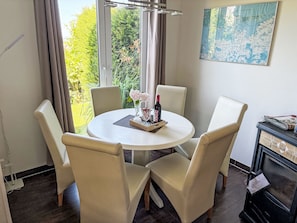 A dining area with a round table, four chairs, a vase with flowers, and a bottle of wine. - Haus Saaler Bodden by Interhome (Neuendorf)