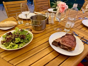 Une table de salle à manger en bois, dressée avec des assiettes remplies de nourriture, notamment un steak et une salade, ainsi que divers verres.
