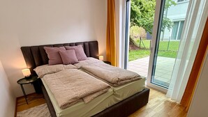 Ein modernes Schlafzimmer mit einem großen Bett, zwei Nachttischen und Blick ins Freie.