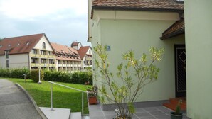 A building with a green facade, a tiled roof, and a small garden area with a bench and potted plants. - mit Gemeinschaftspool und Terrasse by Interhome (Bad Waltersdorf)