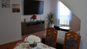 A dining area with a table set for two, a TV mounted on the wall, and a window with curtains. - kunstsammler by Interhome (Dresden)