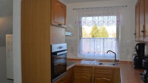 A compact kitchen with wooden cabinets, a built-in oven, a window with lace curtains, and a coffee maker. - kunstsammler by Interhome (Dresden)