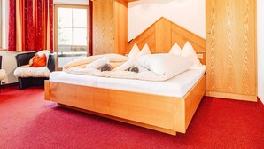 A wooden bed with a sloped headboard in a room with red carpet and red curtains. - Sarah in Galtür by Interhome (Galtür)