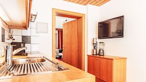 A kitchen with a stainless steel sink, wooden cabinets, a blender, and a television mounted on the wall. - Sarah in Galtür by Interhome (Galtür)