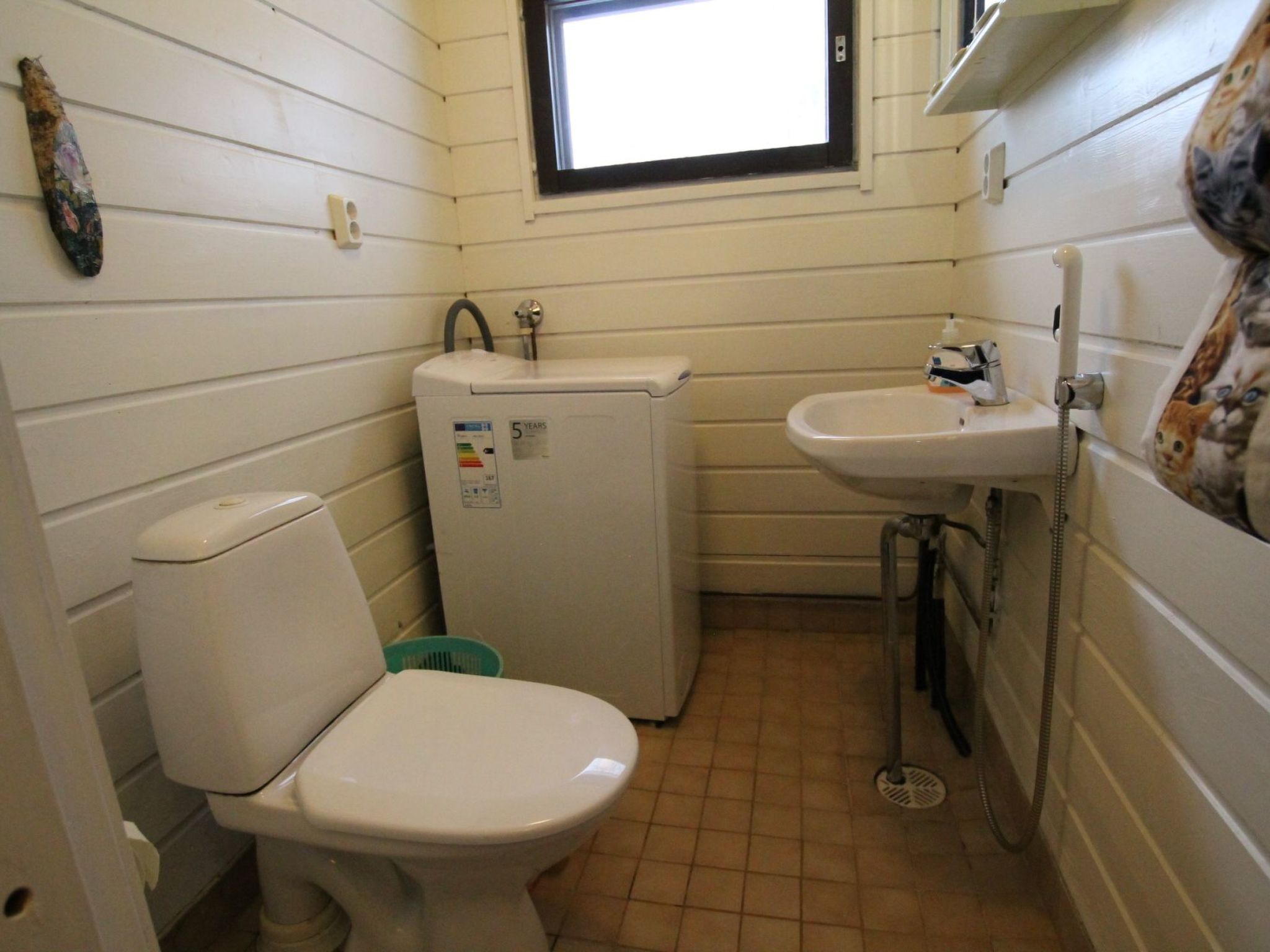 Un baño pequeño con inodoro, un refrigerador compacto, un lavamanos y un ventanal sobre el lavamanos.
