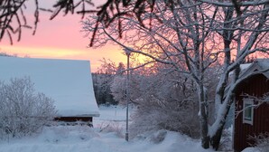 Ett snötäckt landskap med en röd ladugård och ett hus i solnedgången.