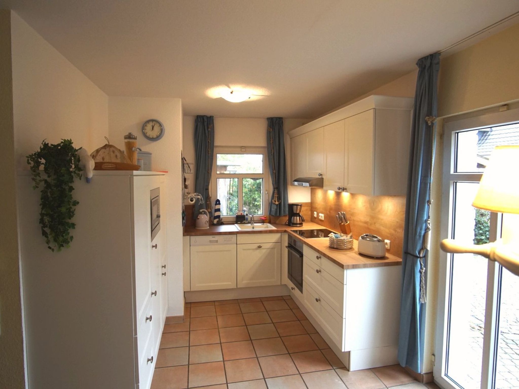 A compact kitchen with white cabinets, a tiled floor, a sink, and a window with curtains.