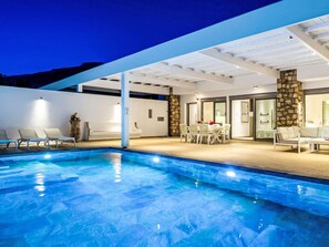 A modern outdoor pool area with a dining table and chairs, a stone pillar, and a covered seating area. - Villa Kleovoulini by Interhome (Pefki)