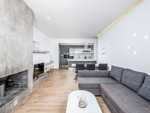 A modern living room with a fireplace, grey sofa, white coffee table, and a kitchen in the background. - Villa Kleovoulini by Interhome (Pefki)