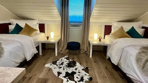 Une chambre avec deux lits, un petit pouf et un tapis en peau de vache.