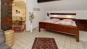 A bedroom with a wooden bed, a small table with a vase, a sofa, and a patterned rug.