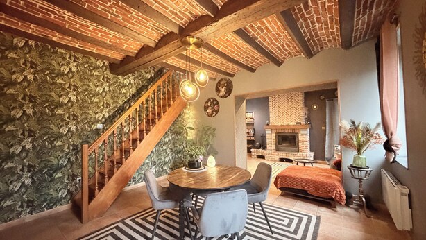Una sala de estar acogedora con chimenea de ladrillo, una escalera y un comedor con alfombra estampada.