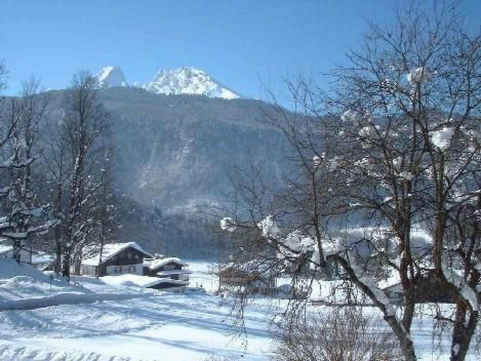 A snow-covered landscape with houses and a mountain in the background.