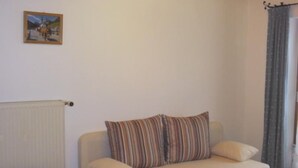 Een knus woongedeelte met een beige bank, gestreepte kussens, een houten bijzettafeltje en een ingelijst schilderij aan de muur.