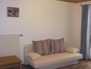 Ein kleiner, gemütlicher Wohnraum mit einem beigefarbenen Sofa, gestreifteren Kissen, einem Holztisch und einem gerahmten Bild an der Wand.