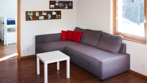 Una sala de estar moderna con un sofá seccional gris, una mesa de centro blanca y suelo de madera. Hay dos paneles con fotografías en la pared y una ventana que ofrece vistas a un paisaje nevado.