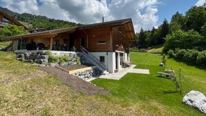 Un chalet de madera con una escalera de piedra, un porche cubierto y vistas a un valle verde.