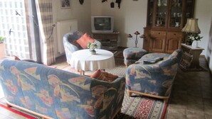 Una sala de estar con sofás estampados, una mesa de centro redonda, un televisor y un mueble con puertas de vidrio.