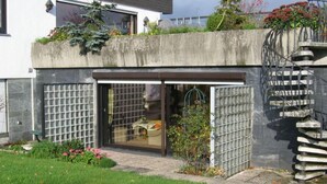 Una casa moderna con puerta de vidrio, fachada de concreto y un pequeño jardín.
