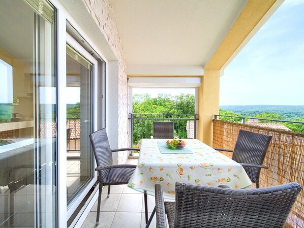 Ein Balkon mit Tisch für zwei Personen, Korbstühlen und Blick auf die grüne Landschaft.