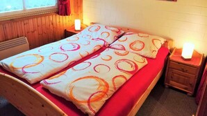 A double bed with a red and white patterned bedspread, two bedside tables with lamps, a window with curtains, and a wall-mounted painting of red flowers. - Vacation home Alissa by Interhome (Extertal)