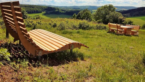 A wooden bench and picnic table set on a grassy hillside with a scenic view of rolling hills and trees in the background. - Vacation home Alissa by Interhome (Extertal)
