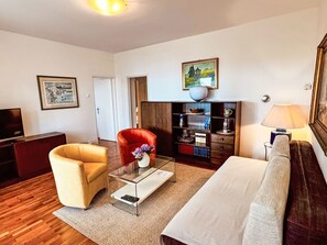 Ein Wohnzimmer mit Sofa, Sessel, Couchtisch, Bücherregal und einem Bild an der Wand.