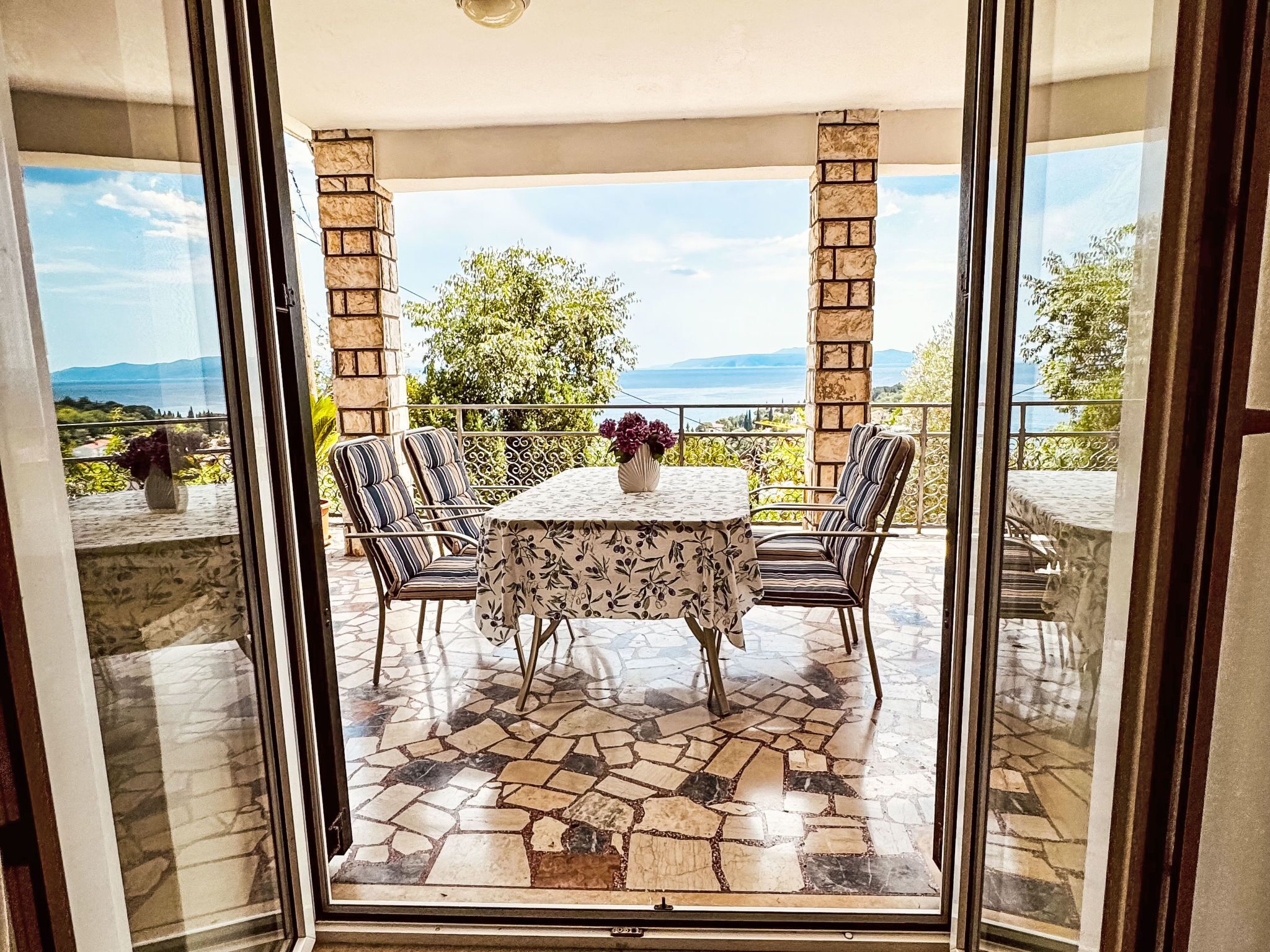 Eine verglaste Terrasse mit Steinboden, einem Tisch und Stühlen sowie Blick auf die Landschaft.