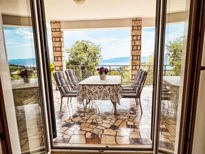 Eine verglaste Terrasse mit Steinboden, einem Tisch und Stühlen sowie Blick auf die Landschaft.