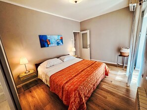 Ein Hotelzimmer mit Bett, einem Bild an der Wand, einer Lampe und einem kleinen Tisch mit einem Korb.
