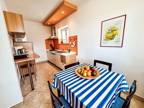 Eine kleine Küche mit Essbereich, mit gestreiftem Tischläufer, Obstschale und einem gerahmten Bild an der Wand.