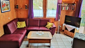 A cozy cabin interior with a red leather sofa, a wooden coffee table, a television, and a bookshelf. - Vacation home Merle by Interhome (Extertal)