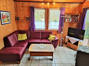 A cozy cabin interior with a red leather sofa, a wooden coffee table, a television, and a bookshelf. - Vacation home Merle by Interhome (Extertal)
